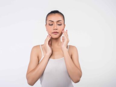 Beautiful young woman with clear fresh skin gently touching her face