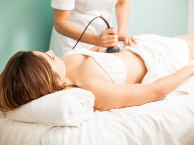 Female therapist performing body contouring treatment on client focusing on abdominal area